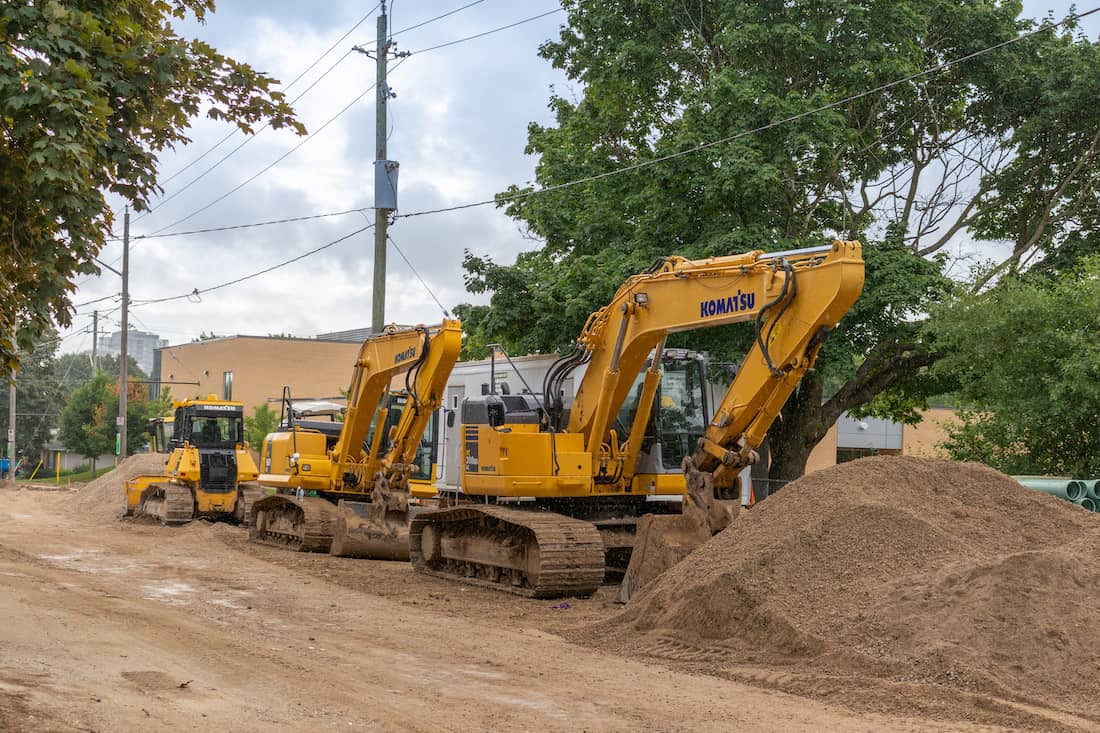 rented excavators in a row with dirt pile